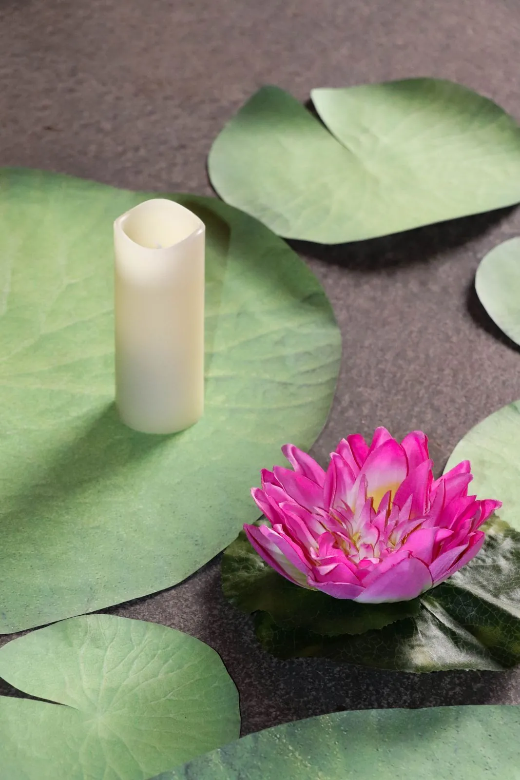 Seerosenblätter mit pinker Seerose und Kerze